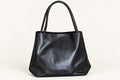 A spacious black tote with a softly structured silhouette, long shoulder handles and an elegant gold-tone zipped front pocket. A refined everyday piece combining minimalist design with practical storage.