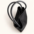 Top view of the black tote bag, showing the open main compartment, folded side construction and long, textured handles.
